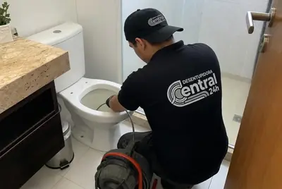 Técnico uniformizado desentupindo um vaso sanitário com máquina profissional